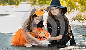 Two little cute girl in witch costume holding jack-o-lantern pumpkin bucket. Kids trick or treating in Halloween holiday
