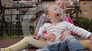 Two little cute girls having great fun while riding down slide in the playground