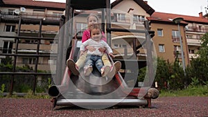 Two little cute girls having great fun while riding down slide in the playground