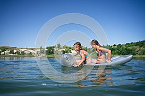 Two little cute girls in swimsuits swim on an inflatable mattress on a blue career lake