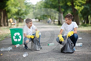 Two little ecologists sitting and collecting plastic rubbish on a blurred park background. Ecology protection concept.