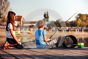 Two little friends, boy and girl fishing on a lake in a sunny summer day