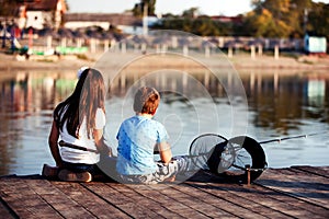 Two little friends, boy and girl fishing on a lake in a sunny summer day