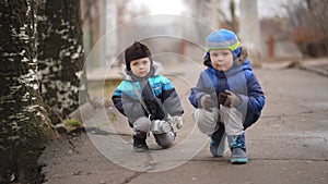 Two little funny baby brothers in baby caps squatting on an alley in the park