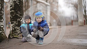 Two little funny baby brothers in baby caps squatting on an alley in the park