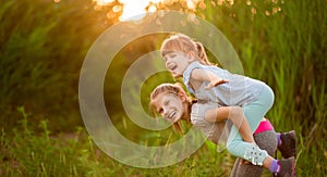 Two little funny sister playing outside on sunset. Little girl climbed up on back of cute sister and fly