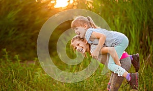 Two little funny sister playing outside on sunset. Little girl climbed up on back of cute sister and fly