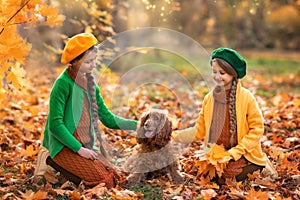 Two little girl children and dog in autumn forest. Female kid and pet portrait at nature with yellow autumn leaves in