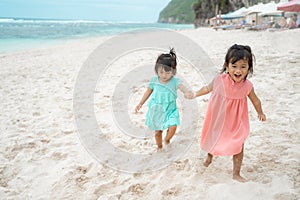 Two little girl hold hand when walking on white sand seashore