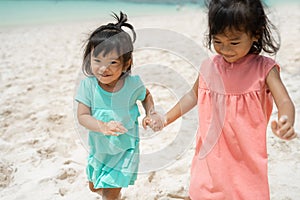 Two little girl hold hand when walking on white sand seashore