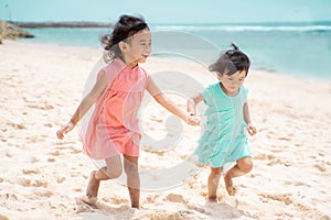 Two little girl hold hand when walking on white sand seashore