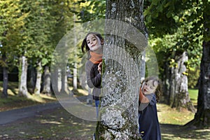 Two little girl looking from behind a tree