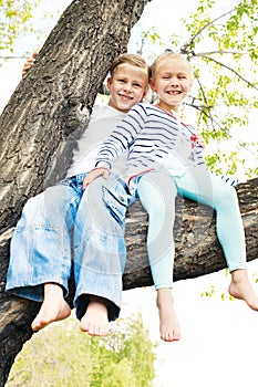 Two little girl sitting on a tree and waving her bare fee