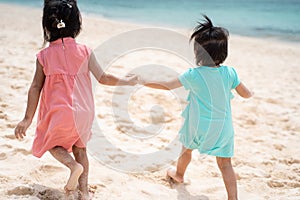 Two little girl walking together on white sand beach from behind view