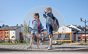 Two little girls with backpacks on the background of the school