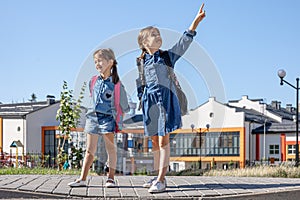 Two little girls with backpacks on the background of the school