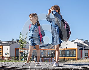 Two little girls with backpacks on the background of the school