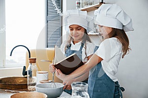 Two little girls in blue chef uniform preparing food on the kitchen and reading receipt book