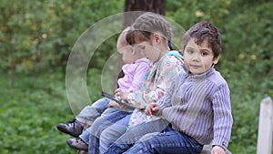 Two little girls and boy play with tablet PC in summer park