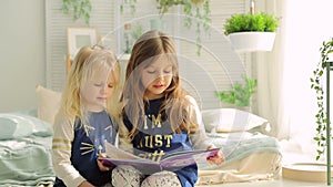 Two little girls in a bright room with plants, read a book