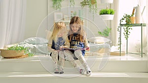 Two little girls in a bright room with plants, read a book