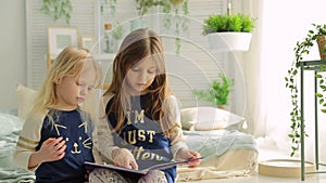 Two little girls in a bright room with plants, read a book