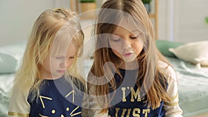 Two little girls in a bright room with plants, read a book