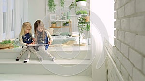 Two little girls in a bright room with plants, read a book