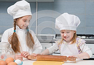 Two little girls in chef uniform sheeted dough