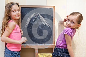 Two little girls draw with chalk on blackboard