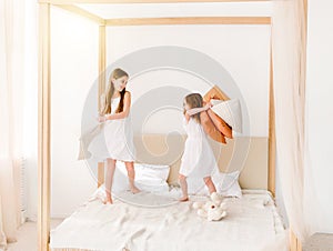 Two little girls fighting with pillows on the bed