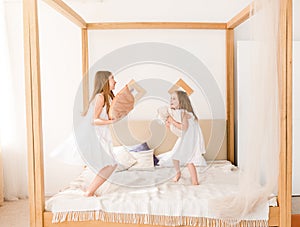 Two little girls fighting with pillows on the bed