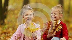 Two little girls are gathering a bouquet of autumn leaves