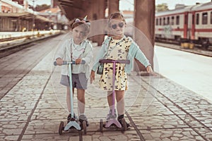 Two little girls having fun with scooters. Sisters play outdoors with scooters