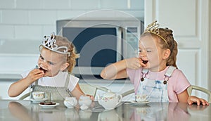 Two little girls having a princess tea party at home. Sibling sister friends wearing tiaras while playing with tea set