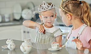 Two little girls having a princess tea party at home. Sibling sister friends wearing tiaras while playing with tea set