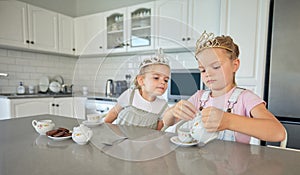 Two little girls having a tea party at home. Sibling sister friends wearing tiaras while playing with tea set and having