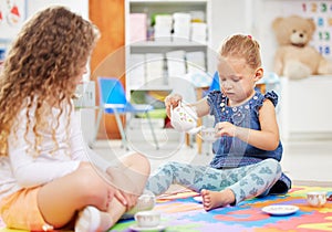 Two little girls having a tea party while playing on a colourful mat on the floor at preschool or kindergarten. Happy
