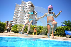 Two little girls holding hands fun jumping into the swimming pool