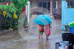 Two little girls holding umbrella and walking along street