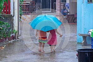 Two little girls holding umbrella and walking along street to ho