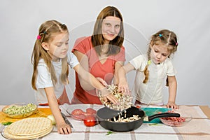Two little girls at kitchen table with a zeal to help her mother pour the mushrooms from the plate to the pan photo