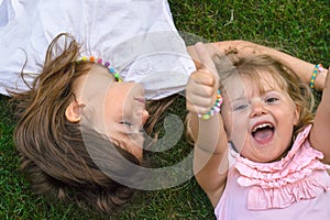Two little girls laying on the grass, laughing and showing thumbs up