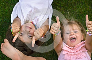 Two little girls laying on the grass, laughing and showing thumbs up