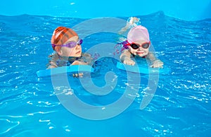 Two little girls learning how to swim in swimming pool using flutter boards