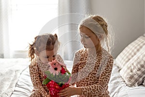 Two little girls in matching pajamas holding flowers to surprise mom