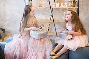 Two little girls in nice pink dresses laugh and open their christmas gifts