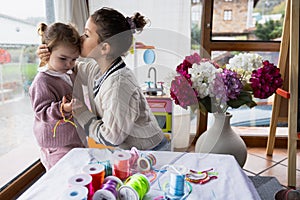 Two little girls, the older one kissing her sister while playing with colored threads