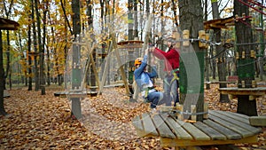 Two little girls in orange helmets in adventure park in safety equipment in autumn  day. Rope Park. rides in the nature. Happiness