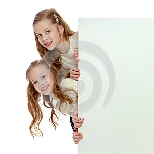 Two little girls peeking out from behind a white advertising ban